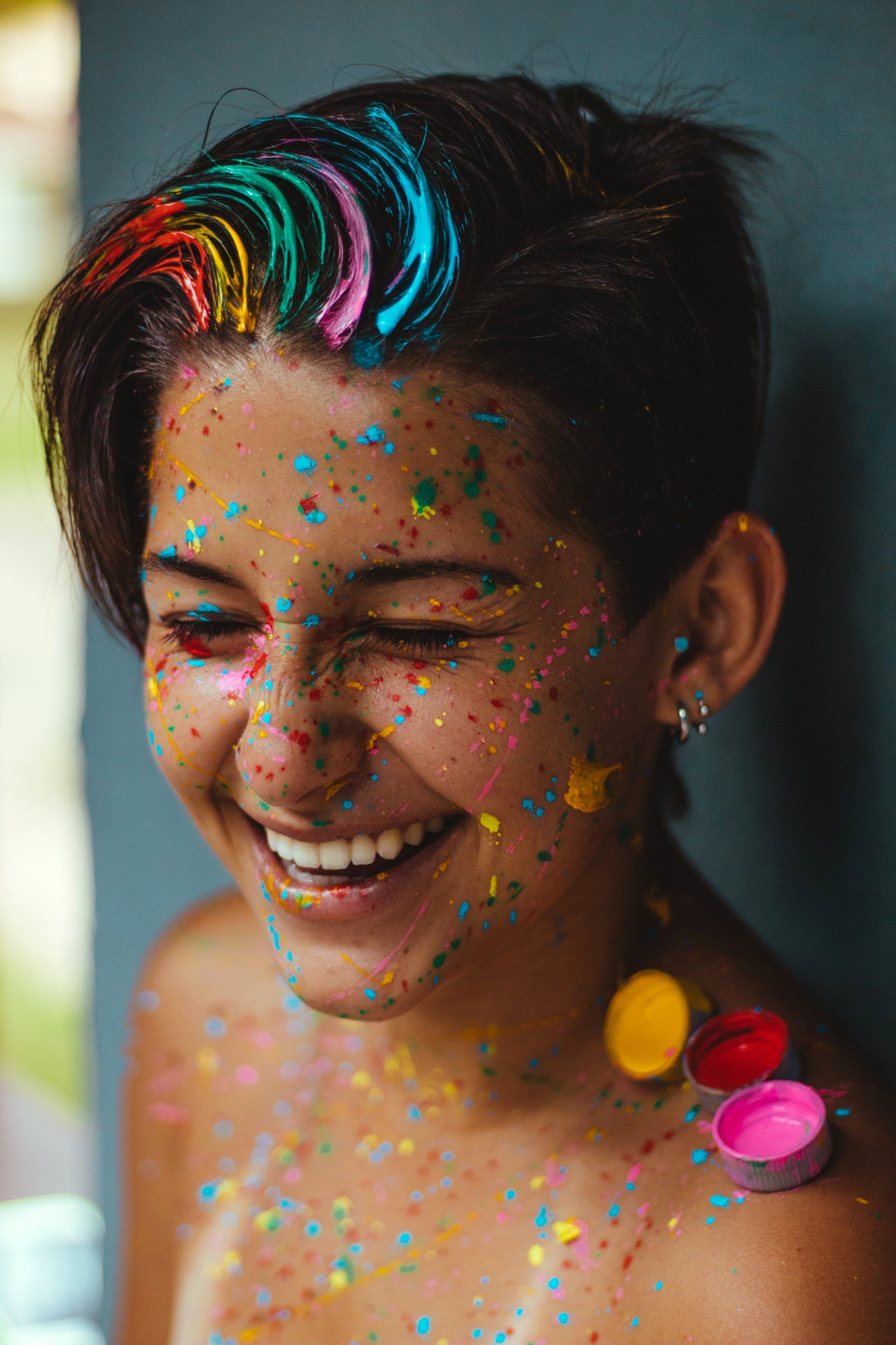 A woman with rainbow hair and confetti on her face is smiling.