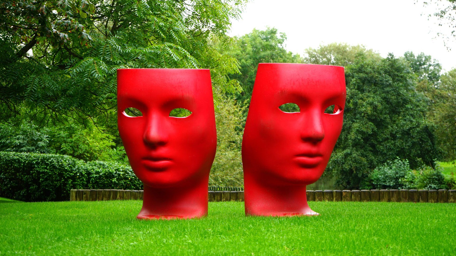 Two red sculptures depicting comedy and drama masks in a field of grass