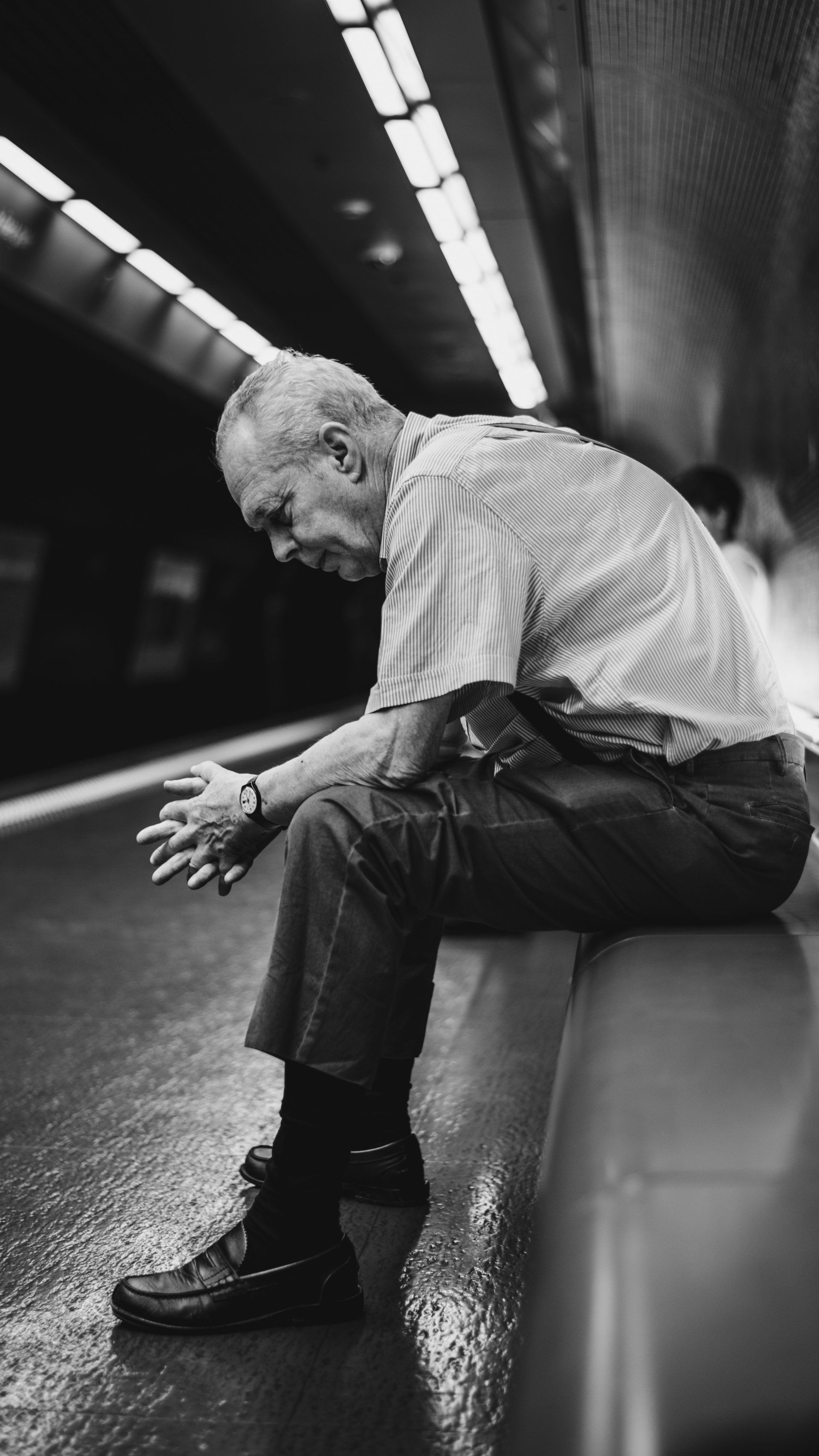 An older man is sitting on a bench in a subway station.