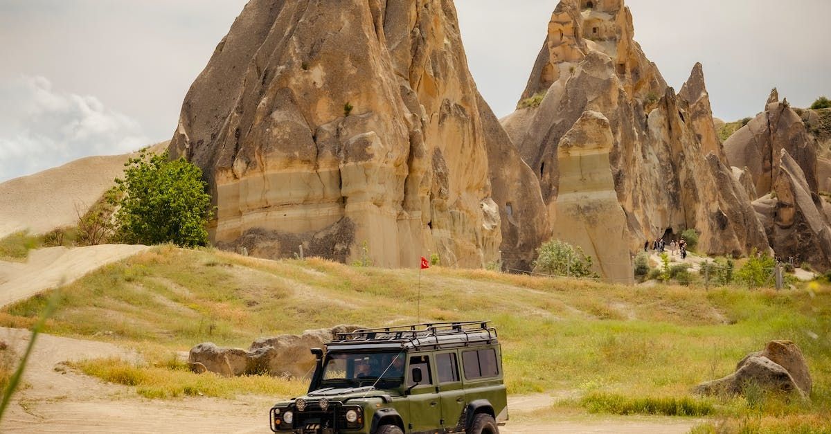 Un defender verde conduce por un camino de tierra frente a una montaña.