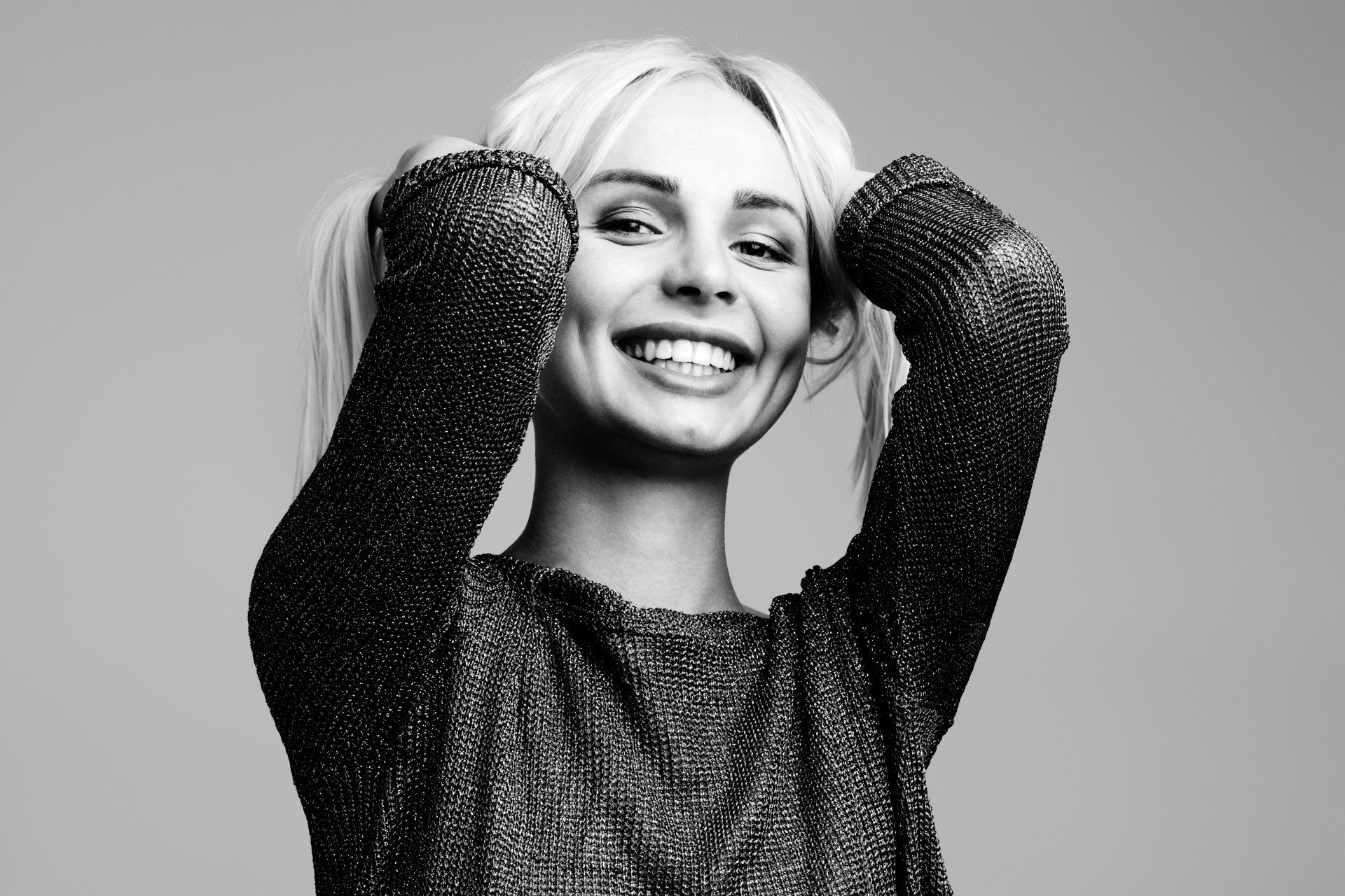 A woman in a sweater is smiling in a black and white photo.