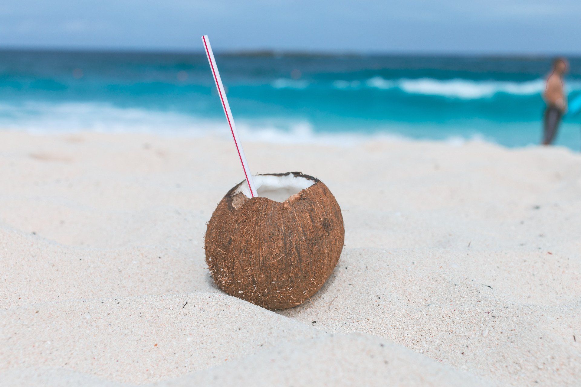 A coconut with a straw in it is on the beach.