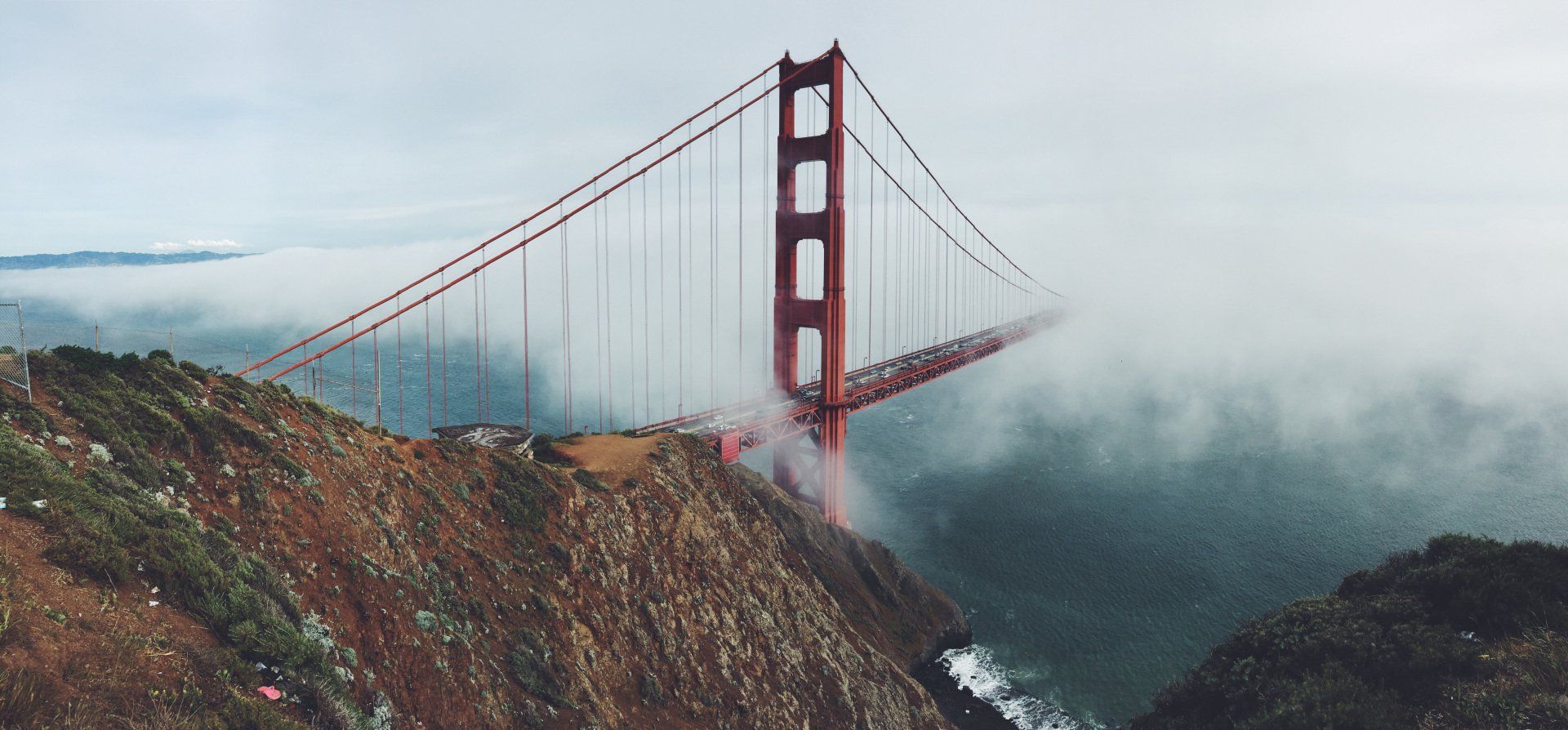 The golden gate bridge is surrounded by fog on a cloudy day.