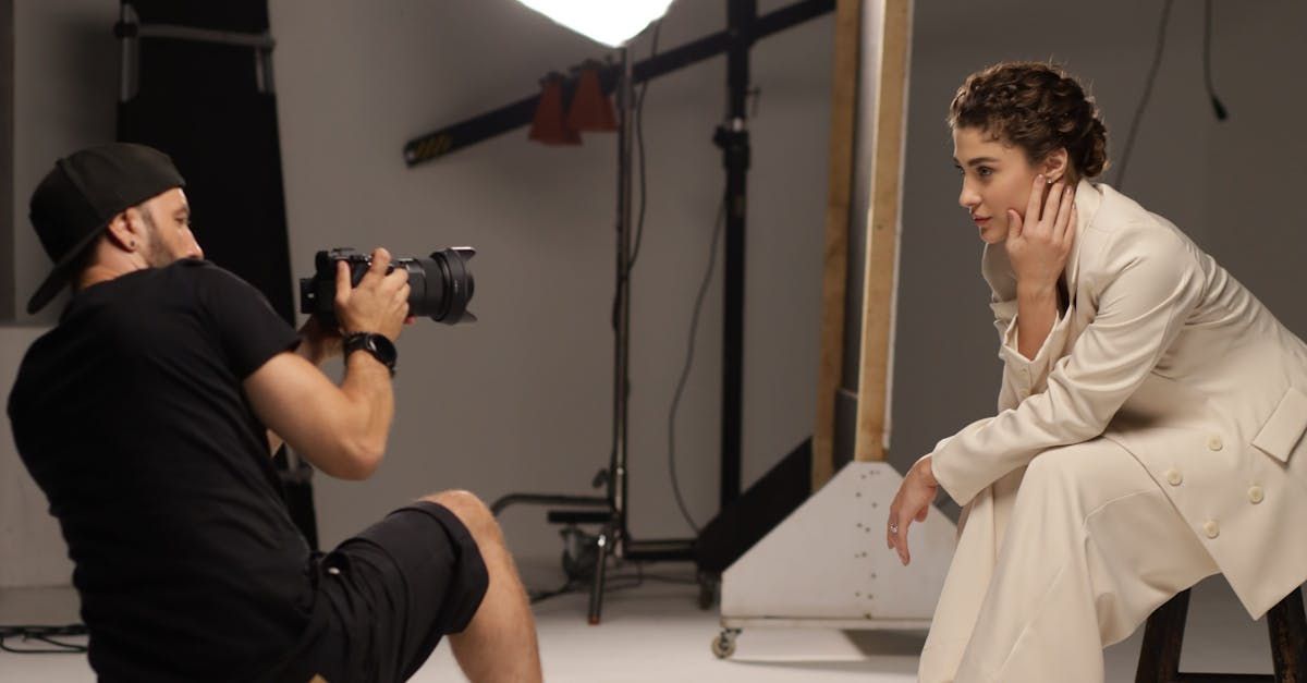 A man is taking a picture of a woman sitting on a stool in a studio.