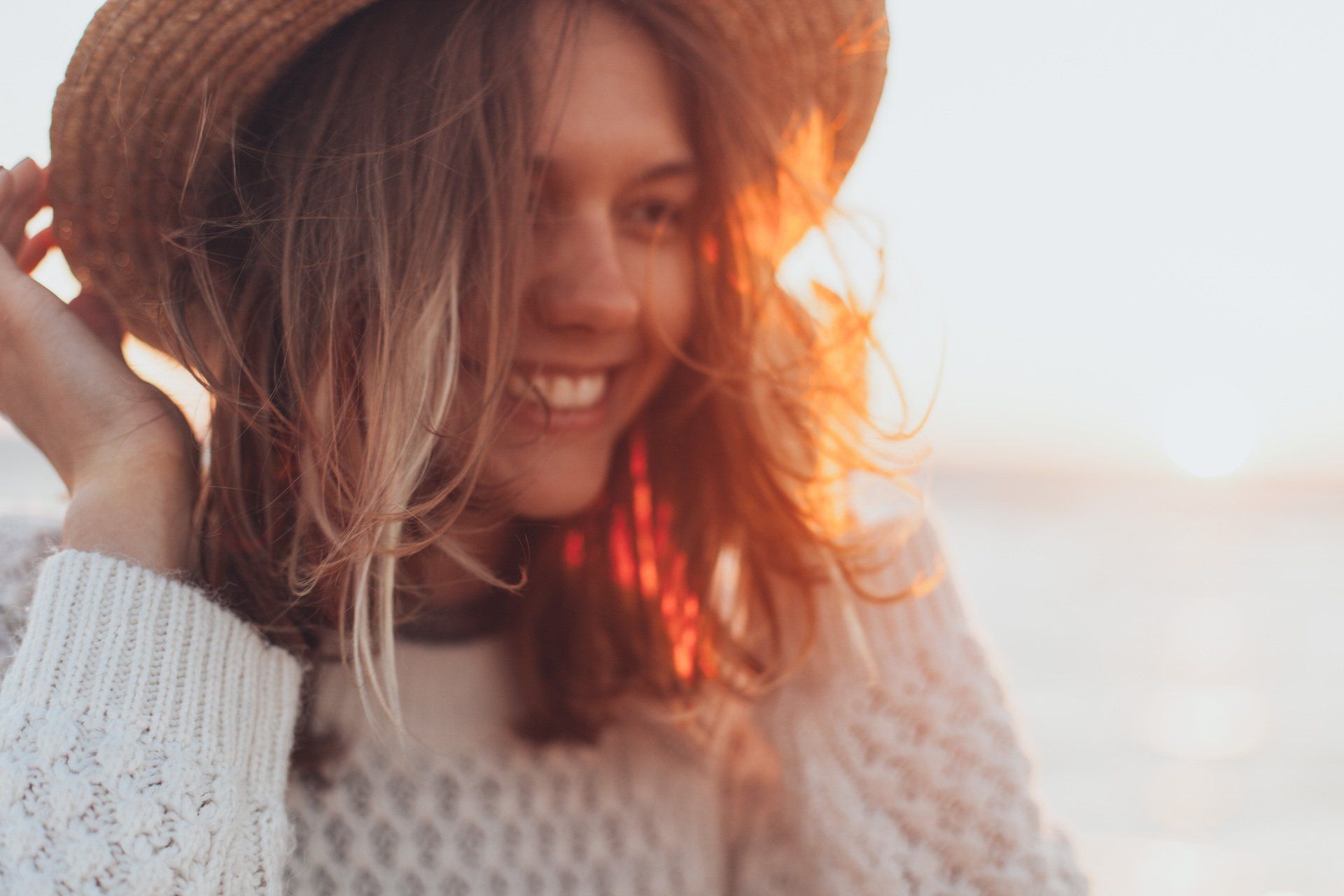 a woman wearing a hat and a white sweater smiles