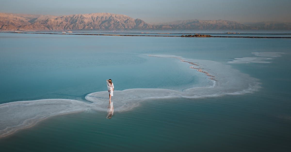 A woman in a white dress is standing in the middle of a body of water.