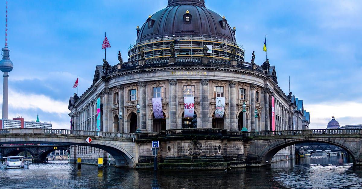 Museum in Berlin mit einer Kuppel davor die Spree neben einer Brücke.
