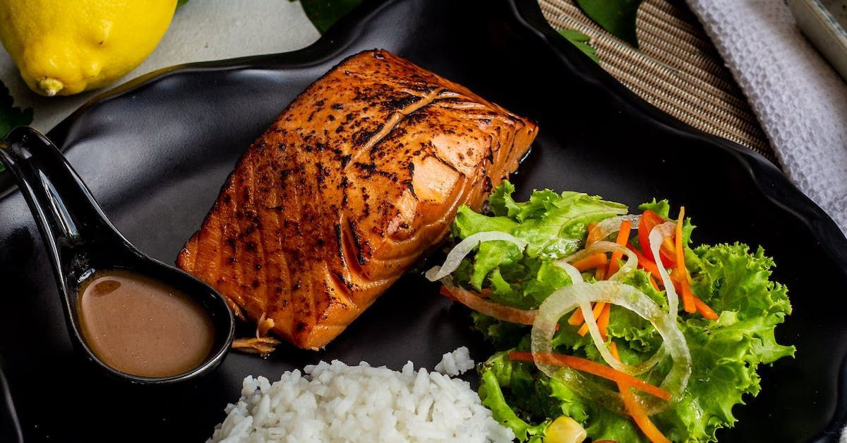 A black plate topped with salmon , rice and vegetables. Nutritional Coaching