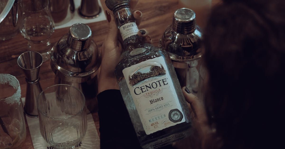A woman is holding a bottle of tequila on a table.