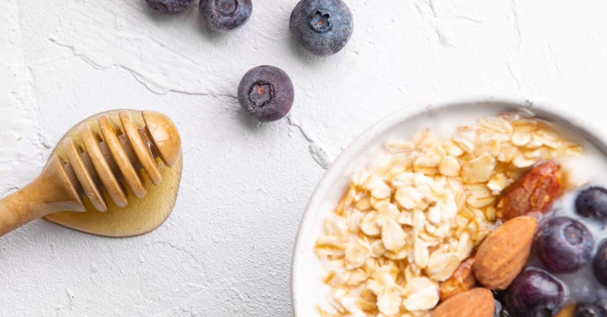A bowl of oatmeal , blueberries , almonds and honey next to a honey dipper.