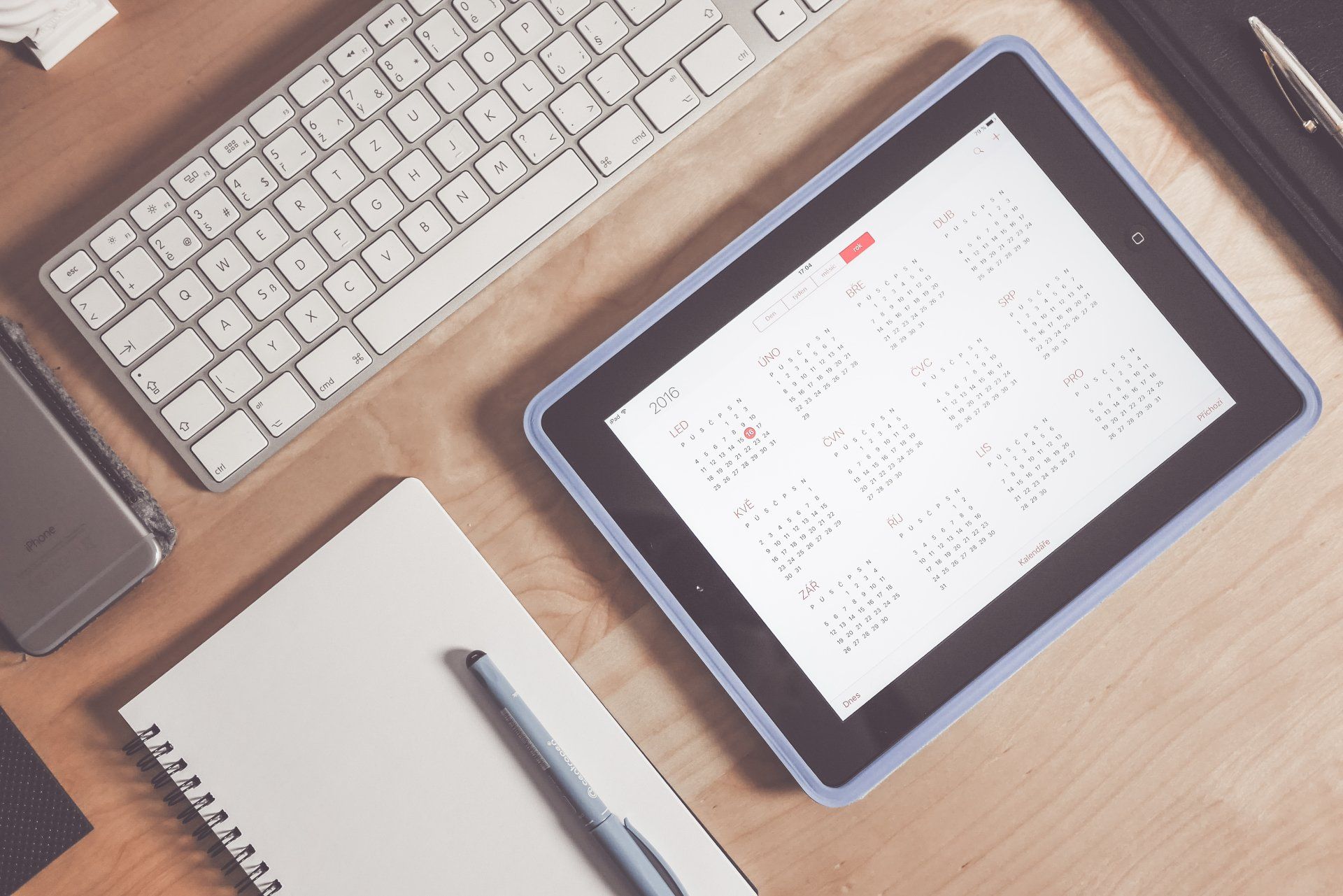 A tablet with a calendar on it sits on a desk next to a keyboard