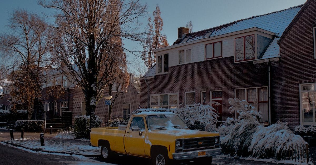 a yellow Chevrolet truck is parked in front of a house in the snow