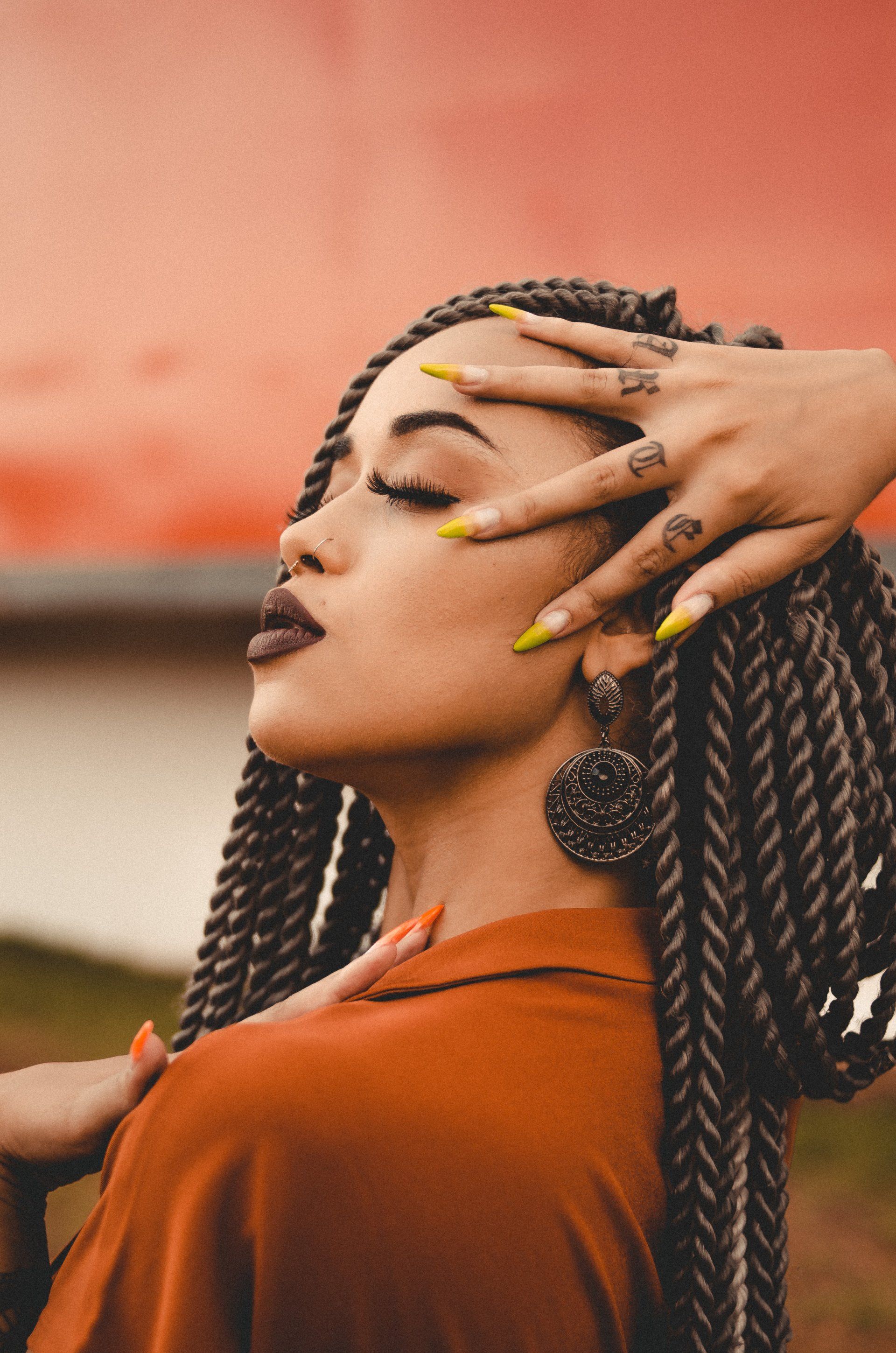A woman with braids and yellow nails is touching her hair.