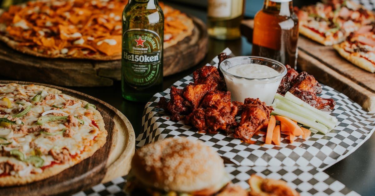 A table topped with pizza , wings , and a bottle of beer.