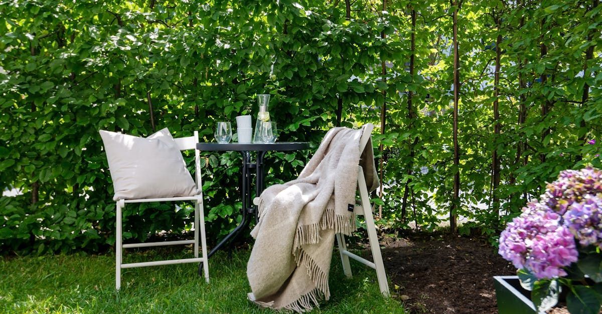 A chair and a table are sitting in the grass in front of a hedge.