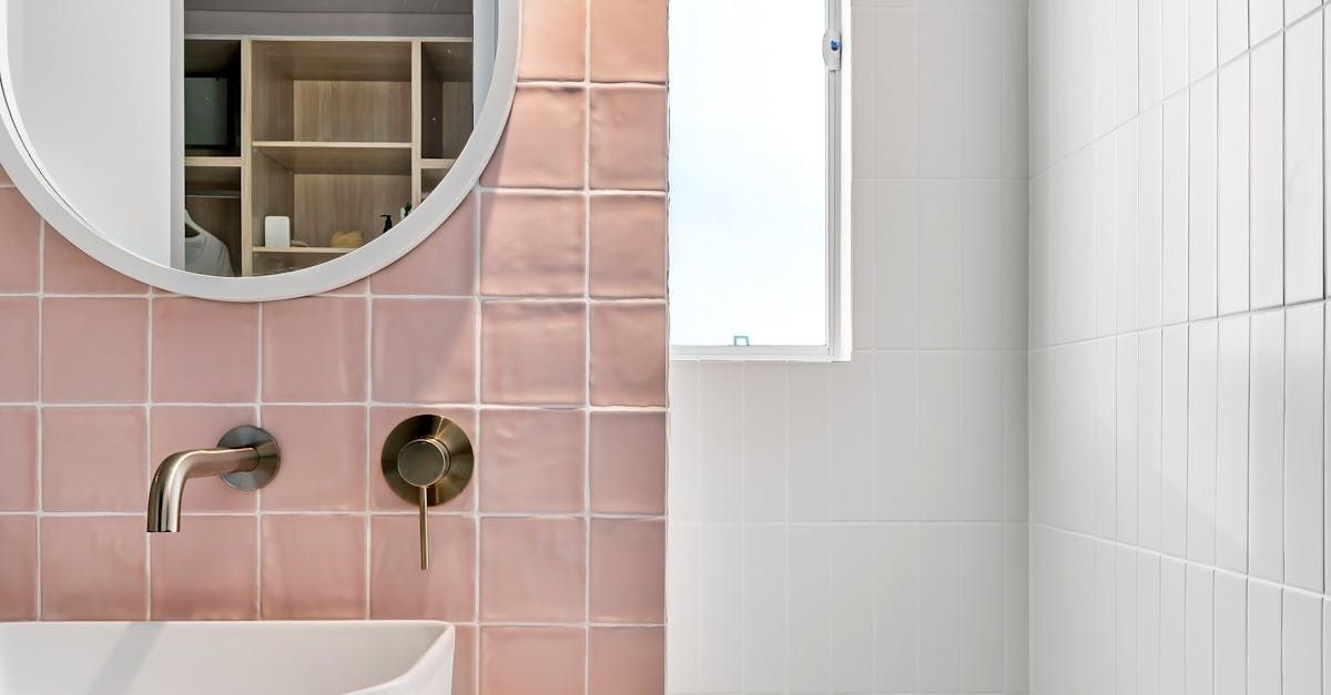 A bathroom with pink tiles , a sink , a mirror and a window.