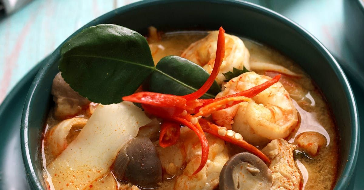 A bowl of soup with shrimp and mushrooms on a table.