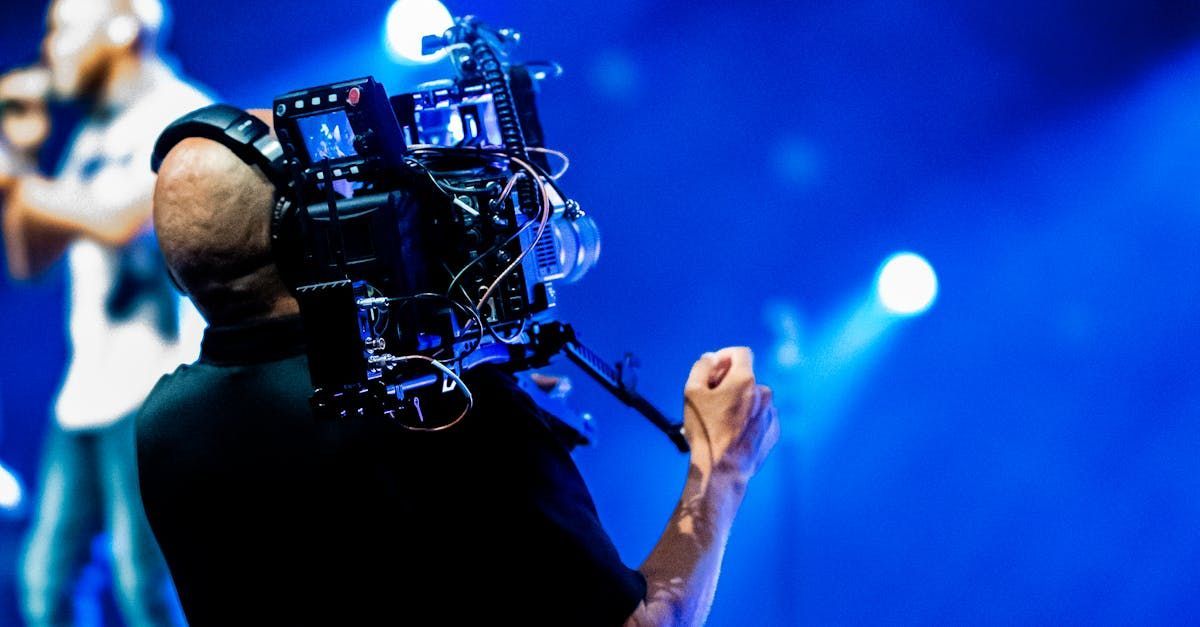 Un homme tient une caméra devant sa tête pendant qu'un homme chante dans un microphone sur scène.