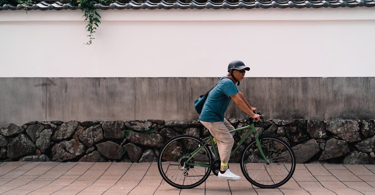 A man is riding a bike on a sidewalk in front of a stone wall.