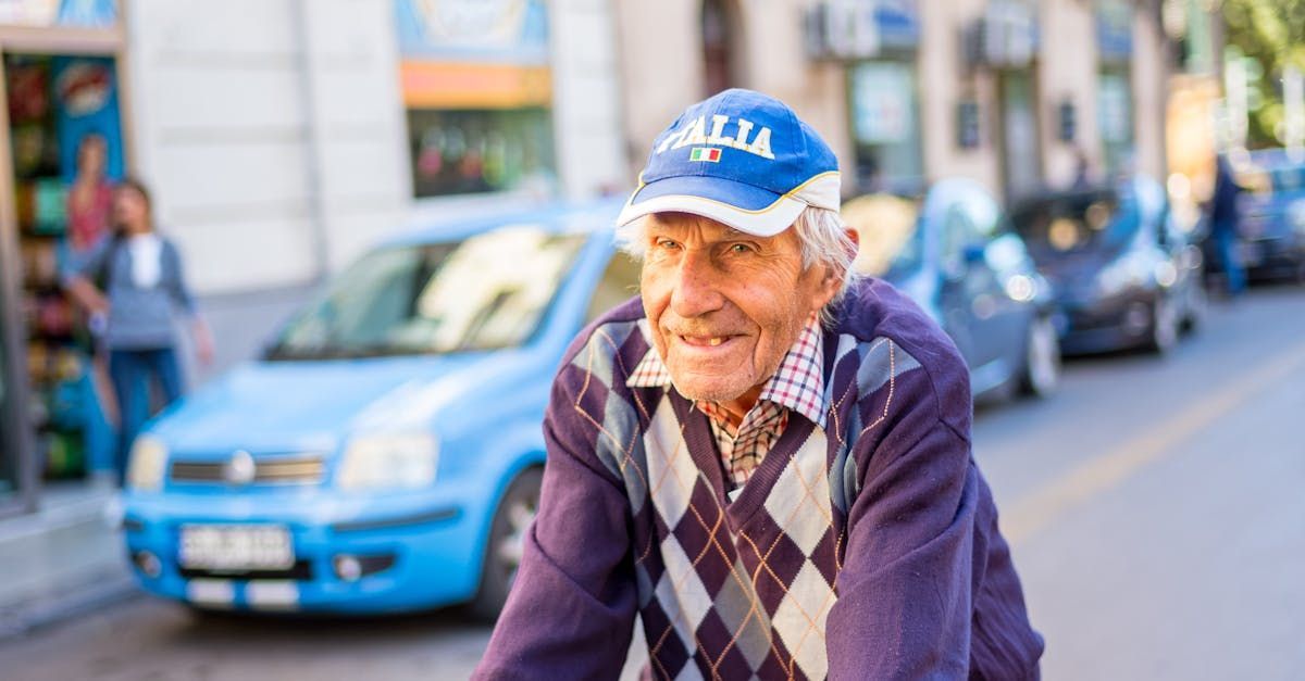 An elderly man wearing a blue hat is riding a bike down a street.