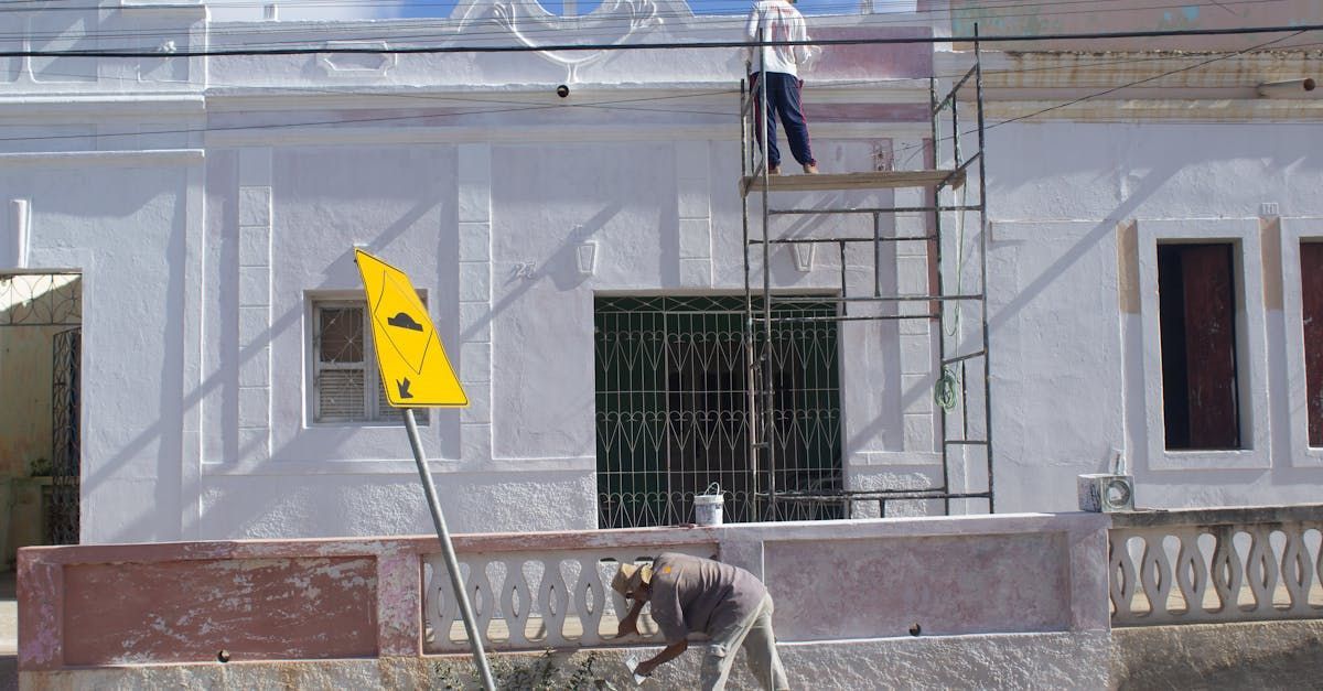 Un homme peint le côté d'un bâtiment blanc.