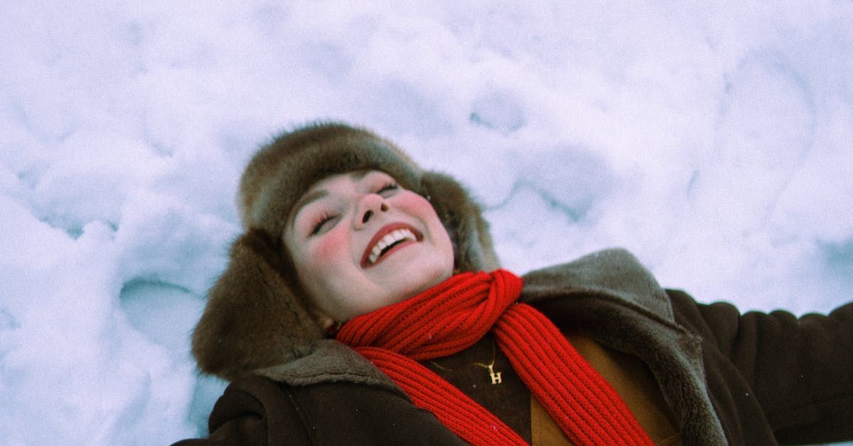 a woman is laying in the snow wearing a fur hat and scarf .