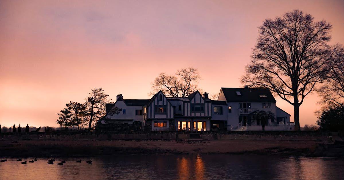 A large house is sitting on the shore of a lake at sunset.