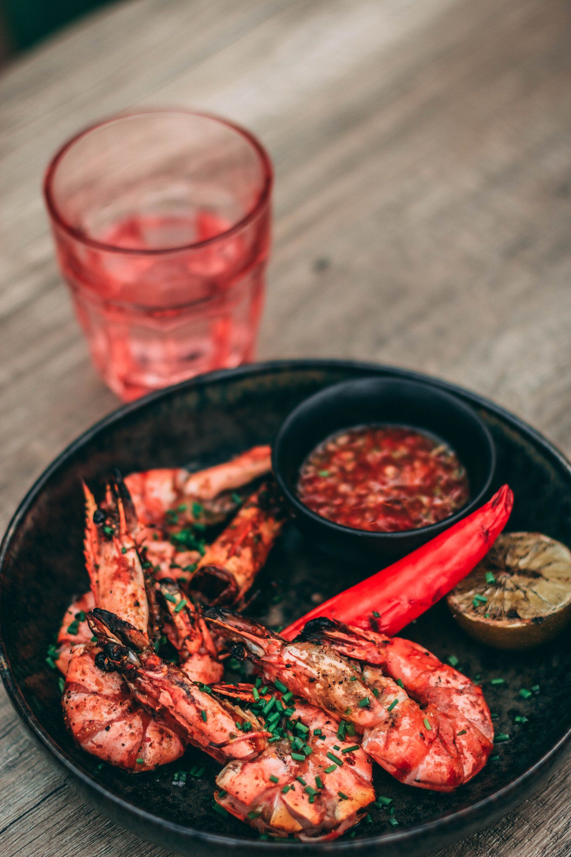 A plate of shrimp with sauce and a glass of water on a table.
