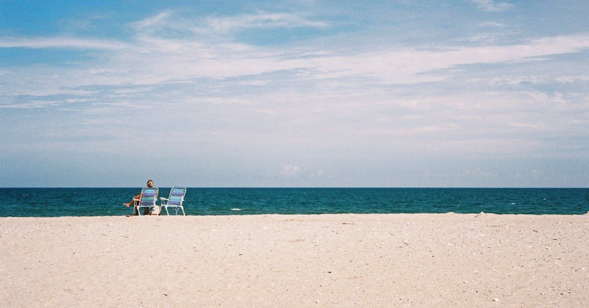 A couple is sitting on a bench on the beach looking at the ocean.