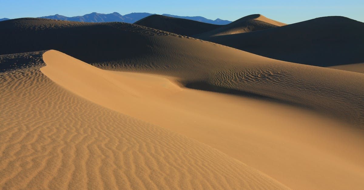 A sand dune in the middle of a desert with mountains in the background.