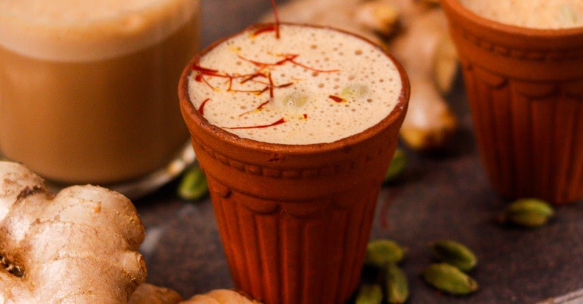 Two cups of tea with ginger and cardamom on a table.