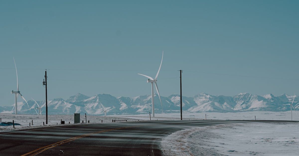 A snowy road with wind turbines in the background and mountains in the background.