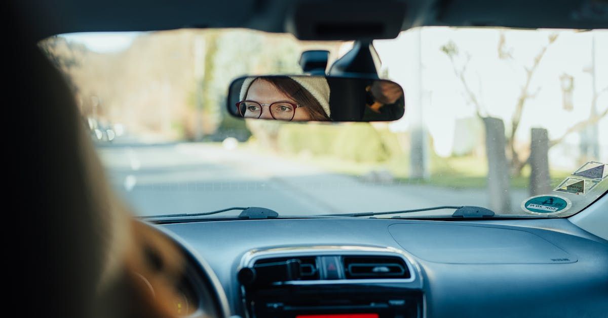 A woman is driving a car and looking at her reflection in the rear view mirror.