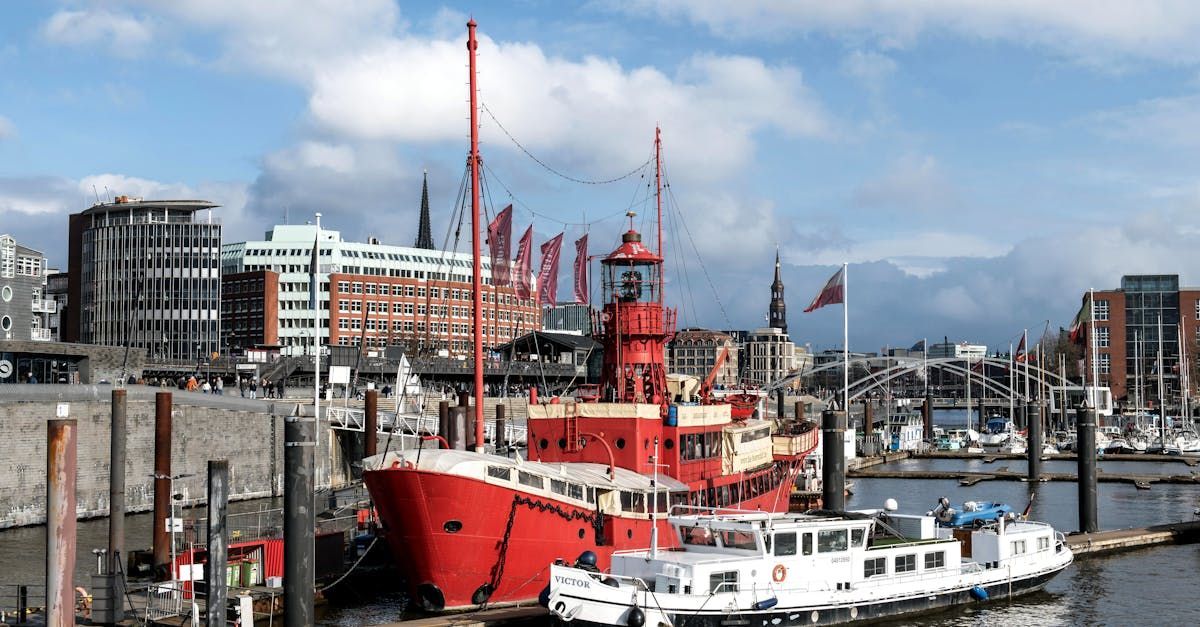 A red boat is docked in a harbor with a city in the background.