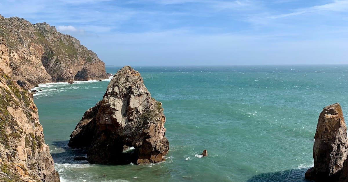 A large rock in the middle of a body of water next to a cliff.