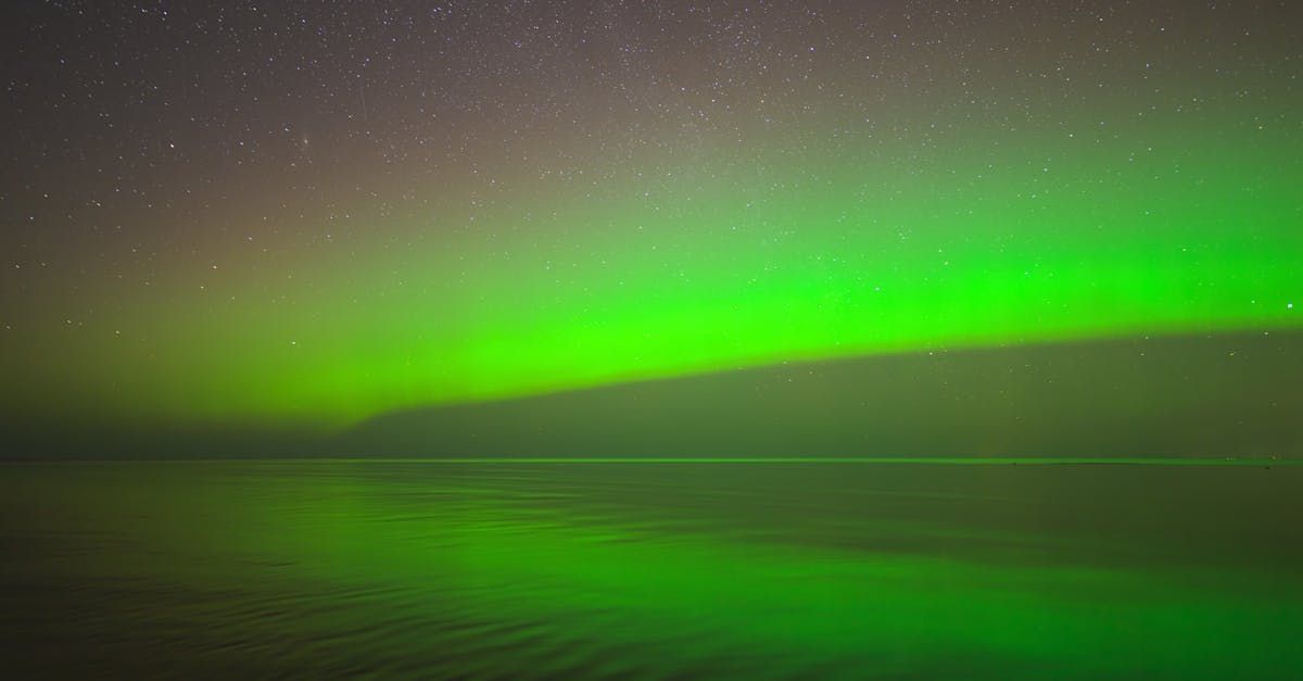 The aurora borealis is glowing brightly in the night sky over a body of water.