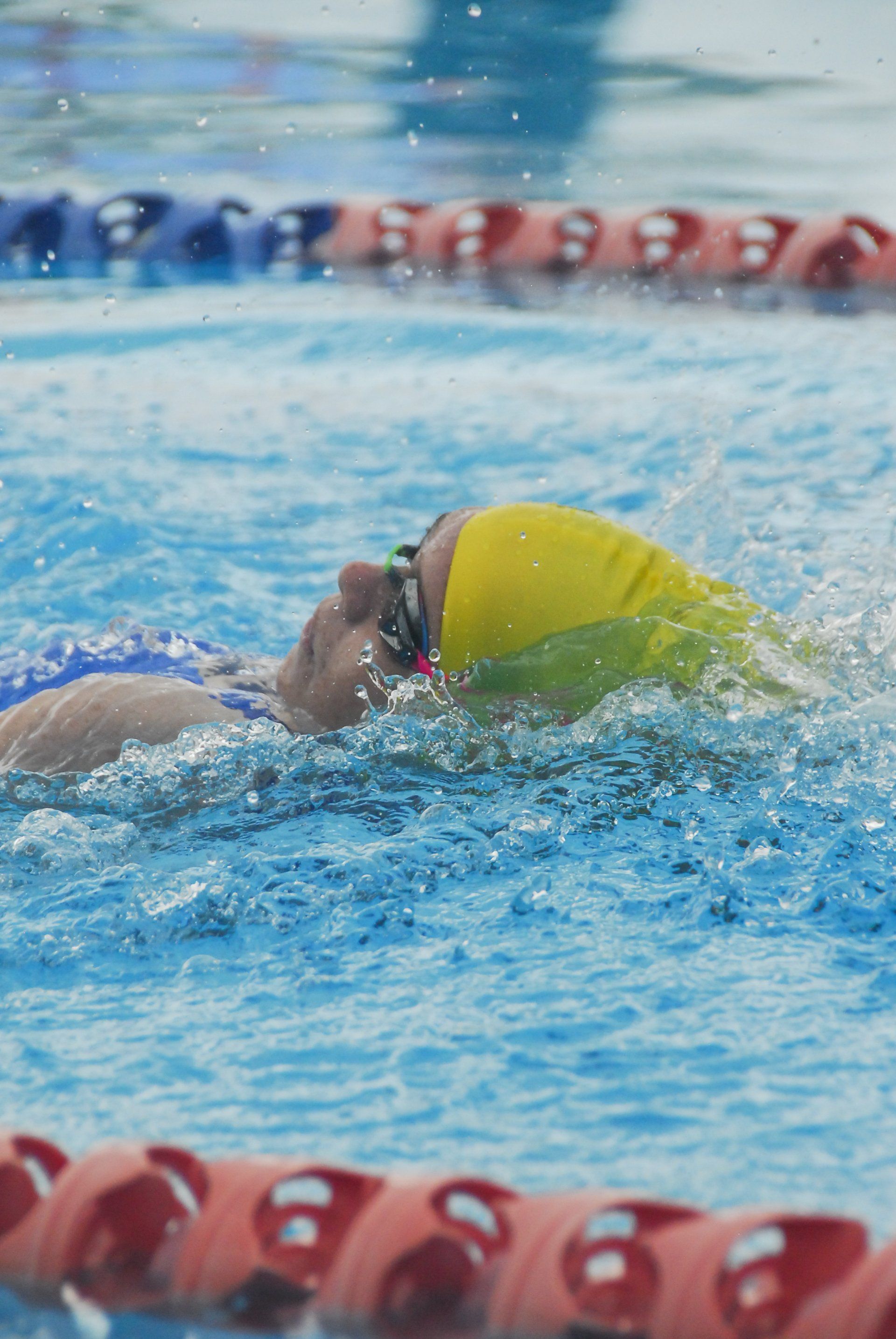 A woman is swimming in a swimming pool wearing a yellow cap and goggles.