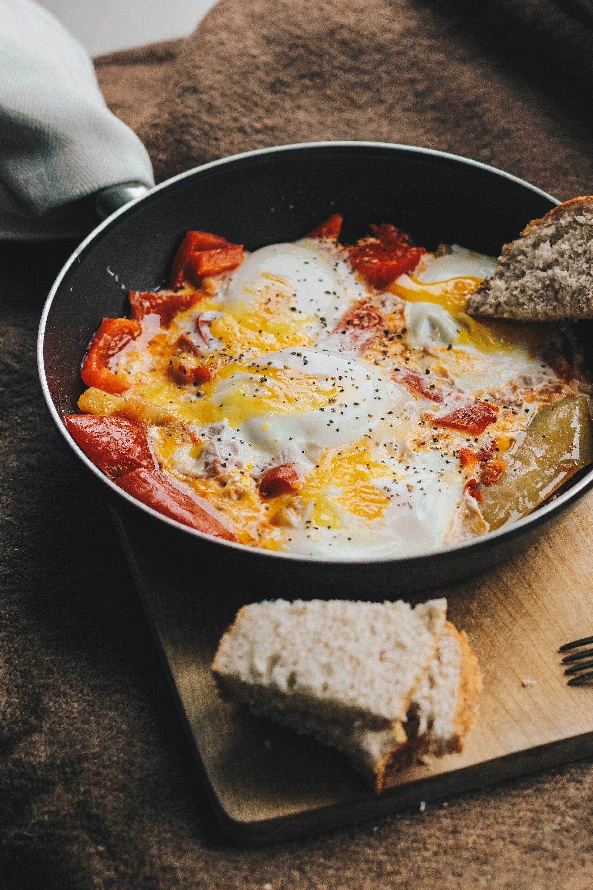 Eggs with red peppers in a pan, served with bread on a wooden board.