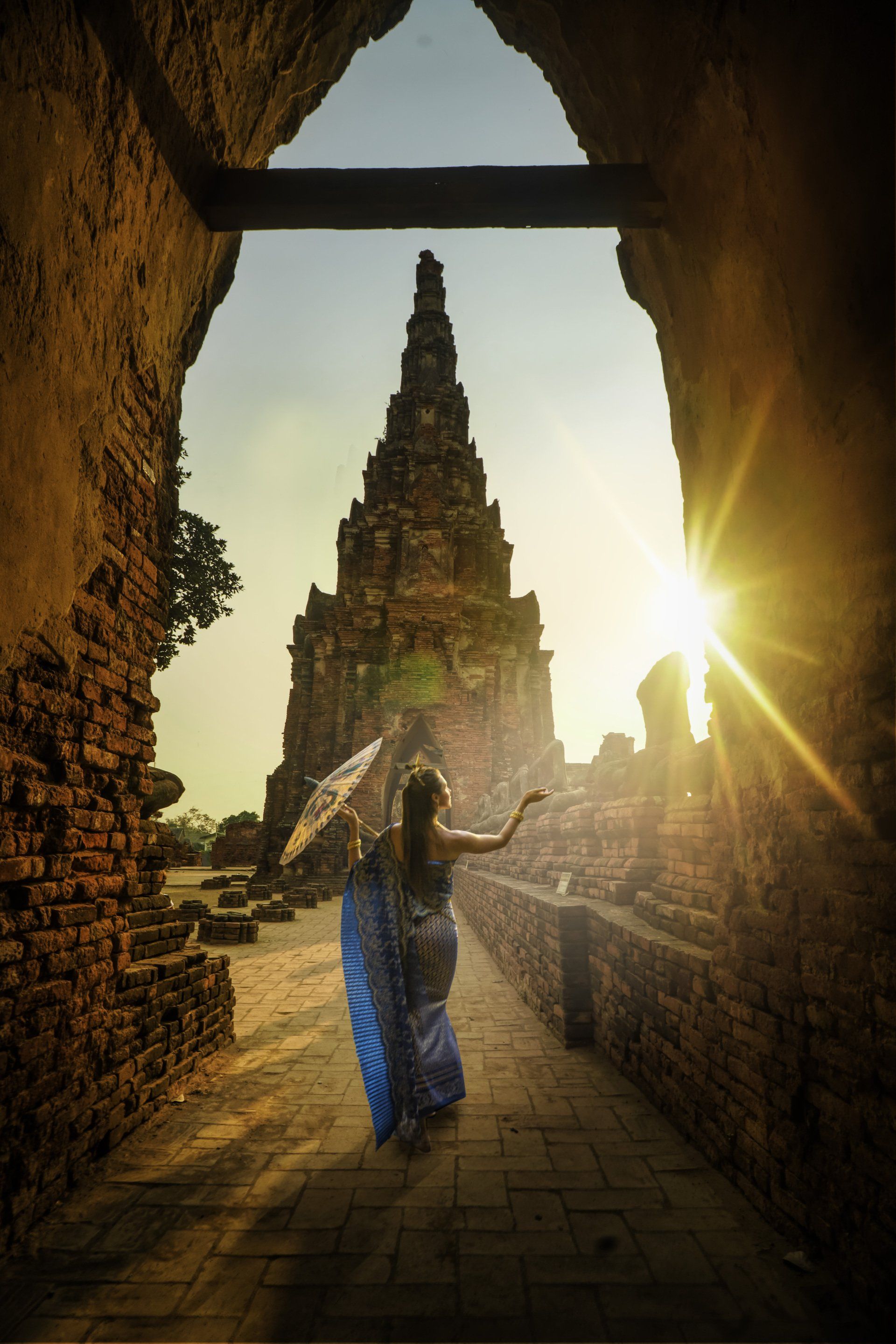 A woman in a blue dress is walking through a tunnel towards a temple.