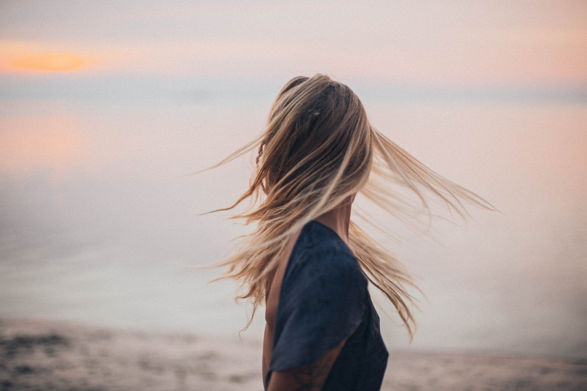 une femme se tient sur la plage avec les cheveux soufflant dans le vent