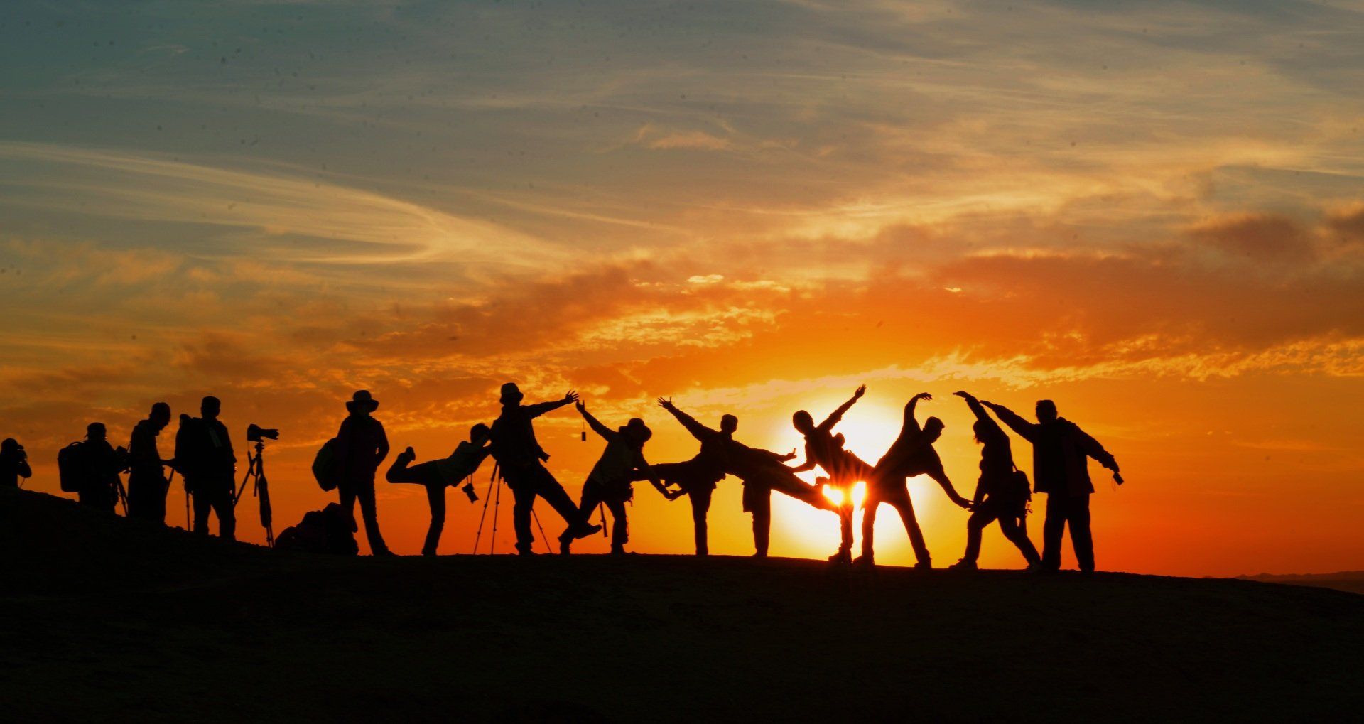 A group of people are standing in a row holding hands at sunset.