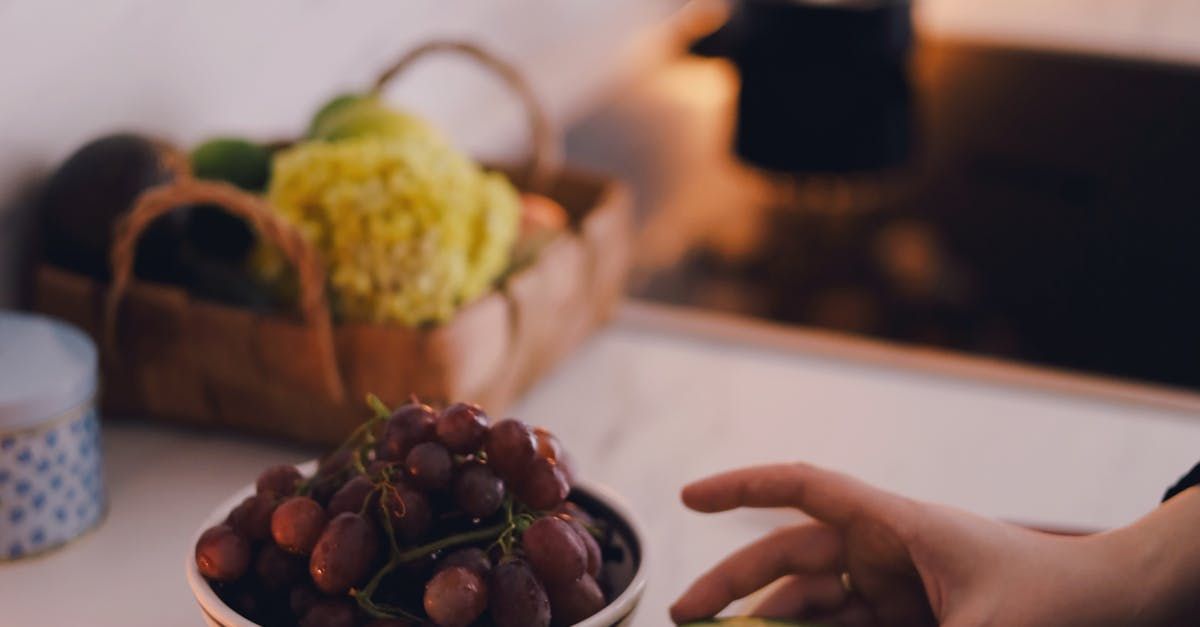 A person is picking grapes from a bowl on a counter.