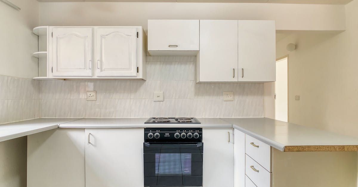 An empty kitchen with white cabinets , a stove , and a microwave.
