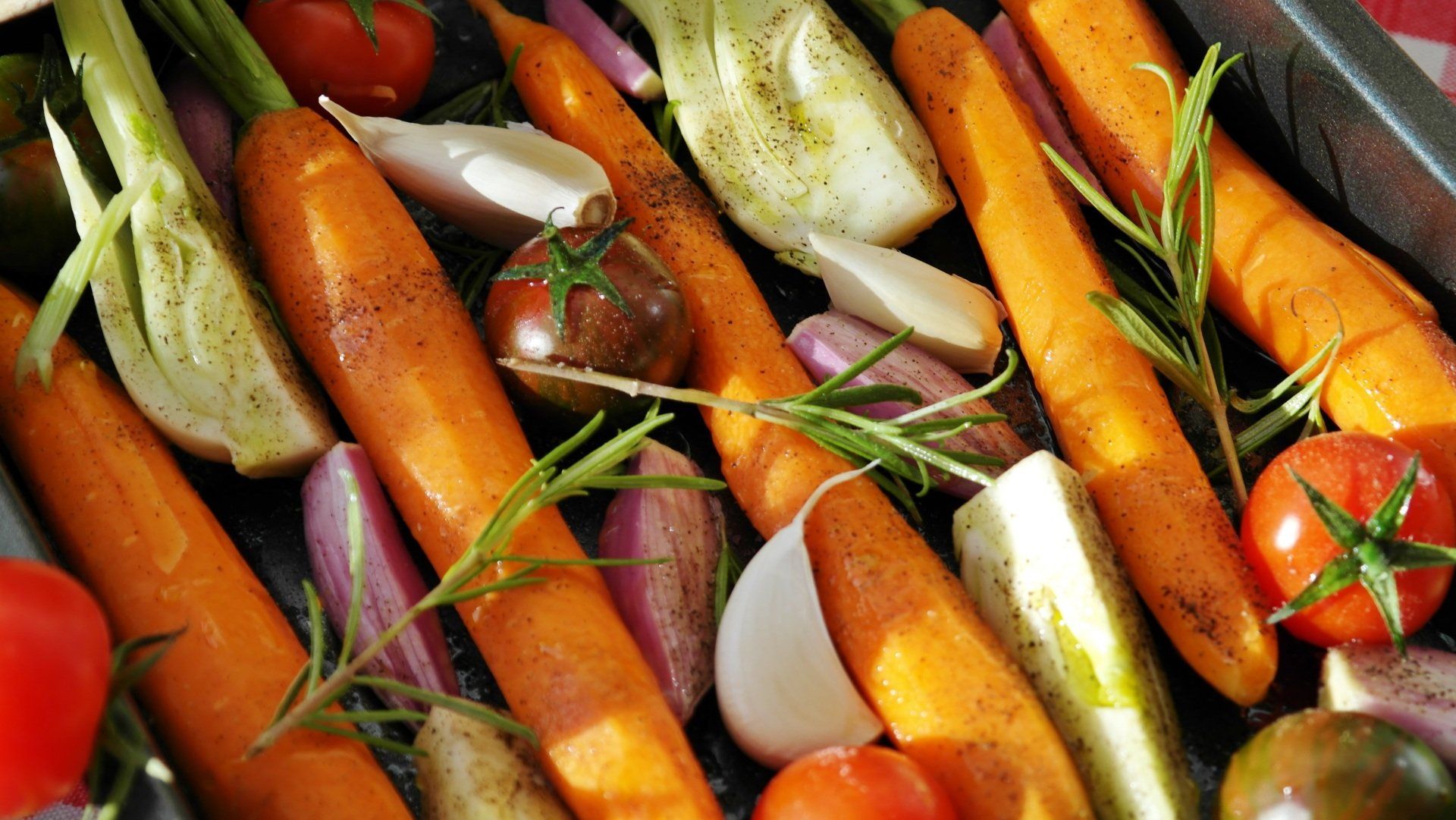 A pan filled with carrots , tomatoes , onions , garlic and other vegetables.