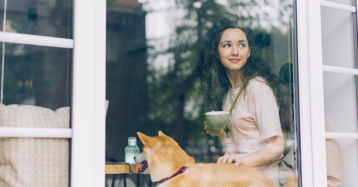 A woman is standing next to a dog in front of a window.