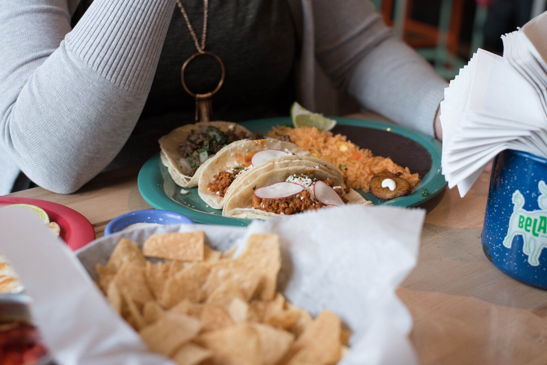 A woman is sitting at a table with a plate of tacos and chips.