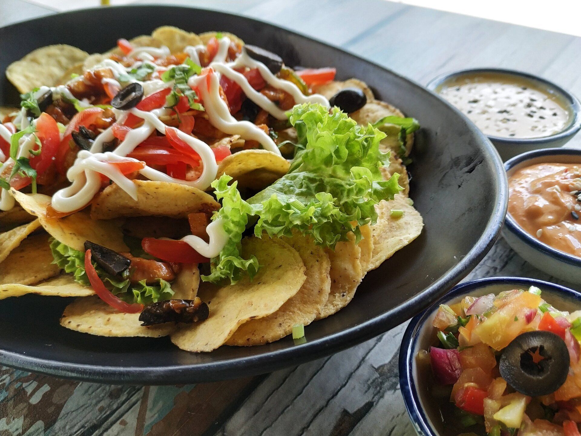 a black plate topped with nachos and salsa on a wooden table .
