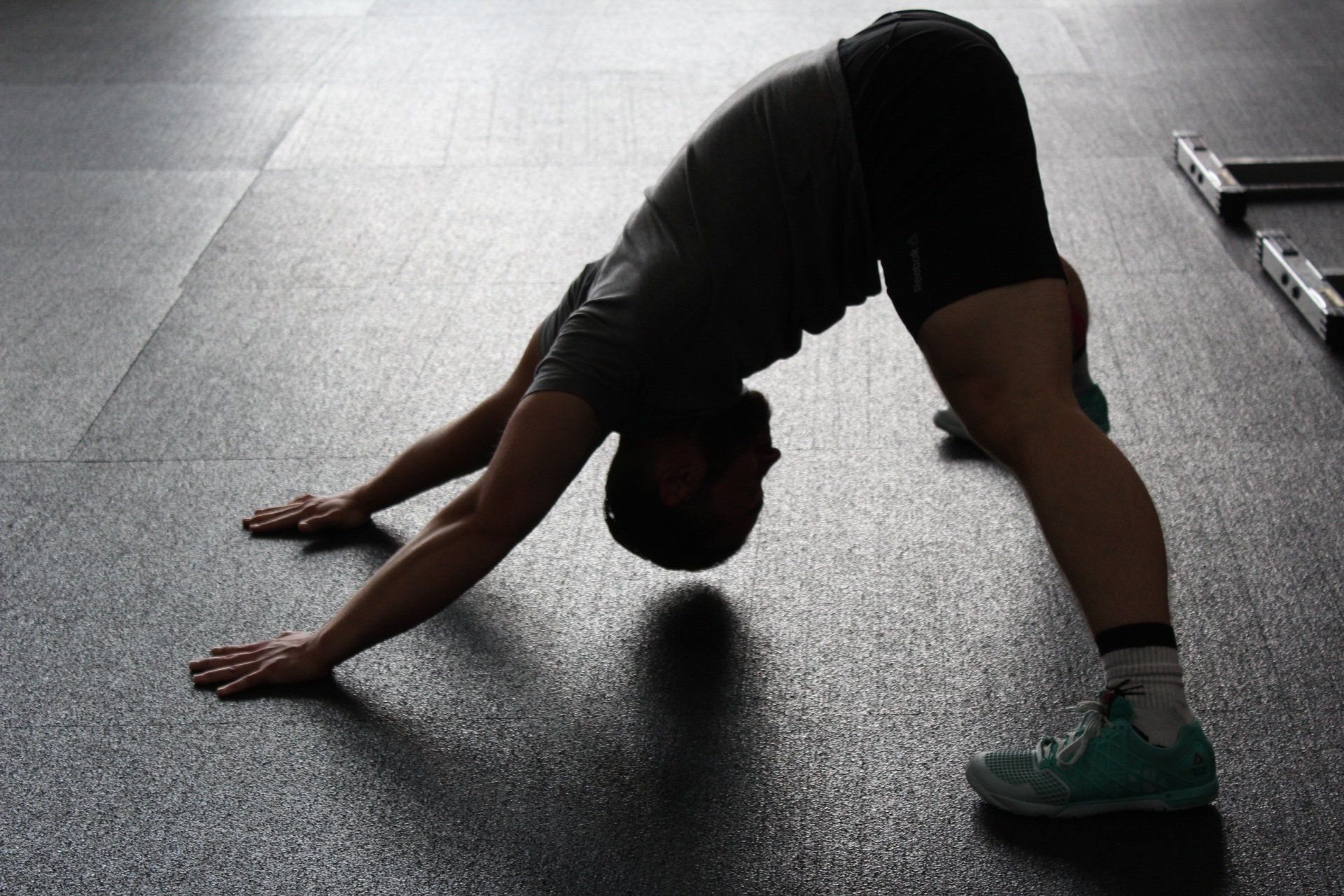 A man is doing a yoga pose on the floor in a gym.