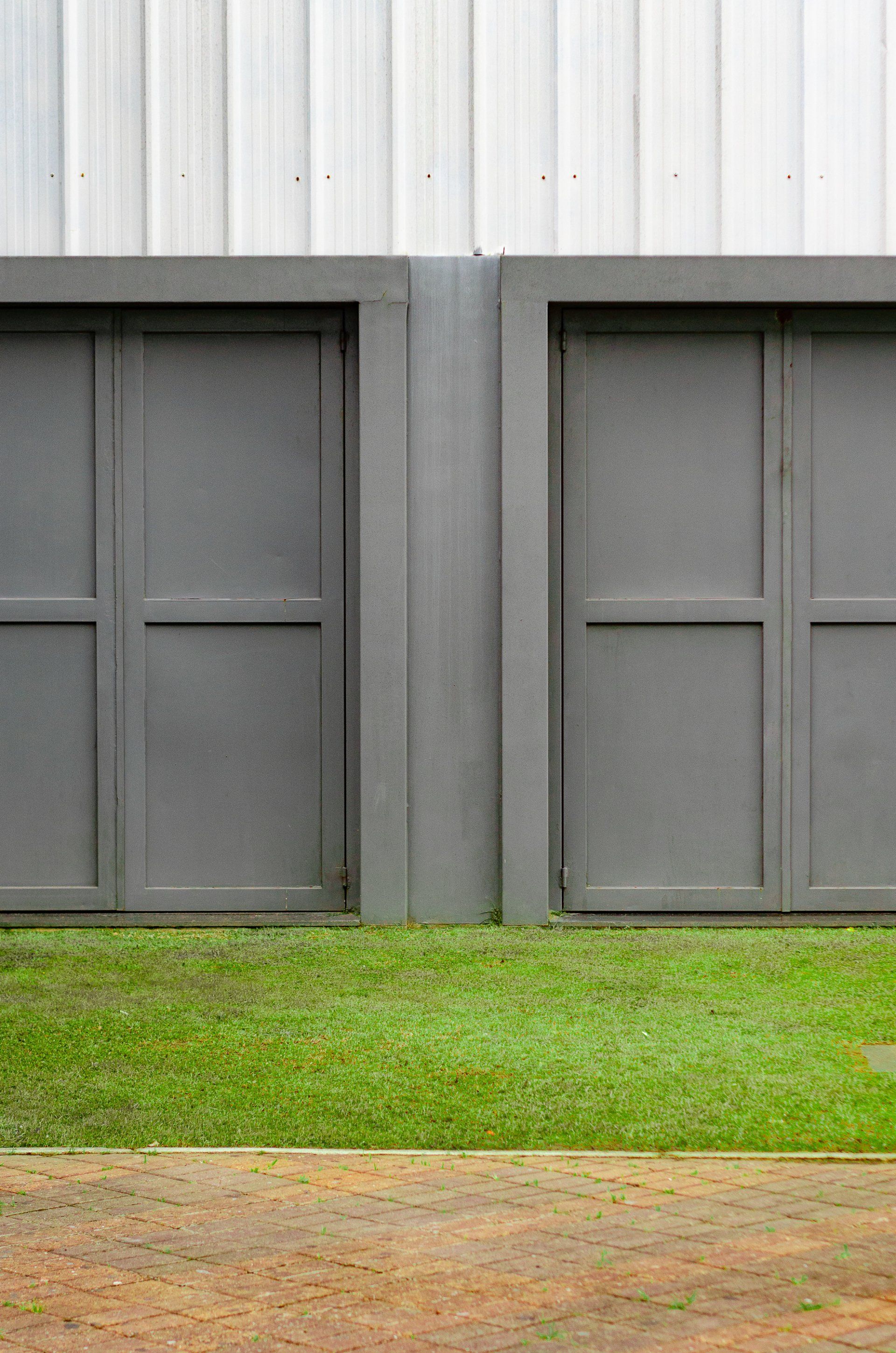 two gray garage doors are sitting next to each other in front of a white building .
