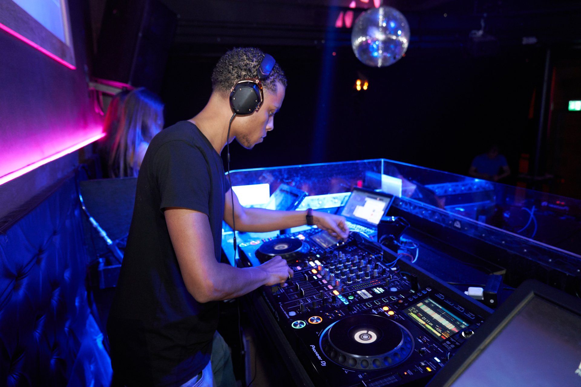 A DJ with headphoes on, turning the dials to adjust the music